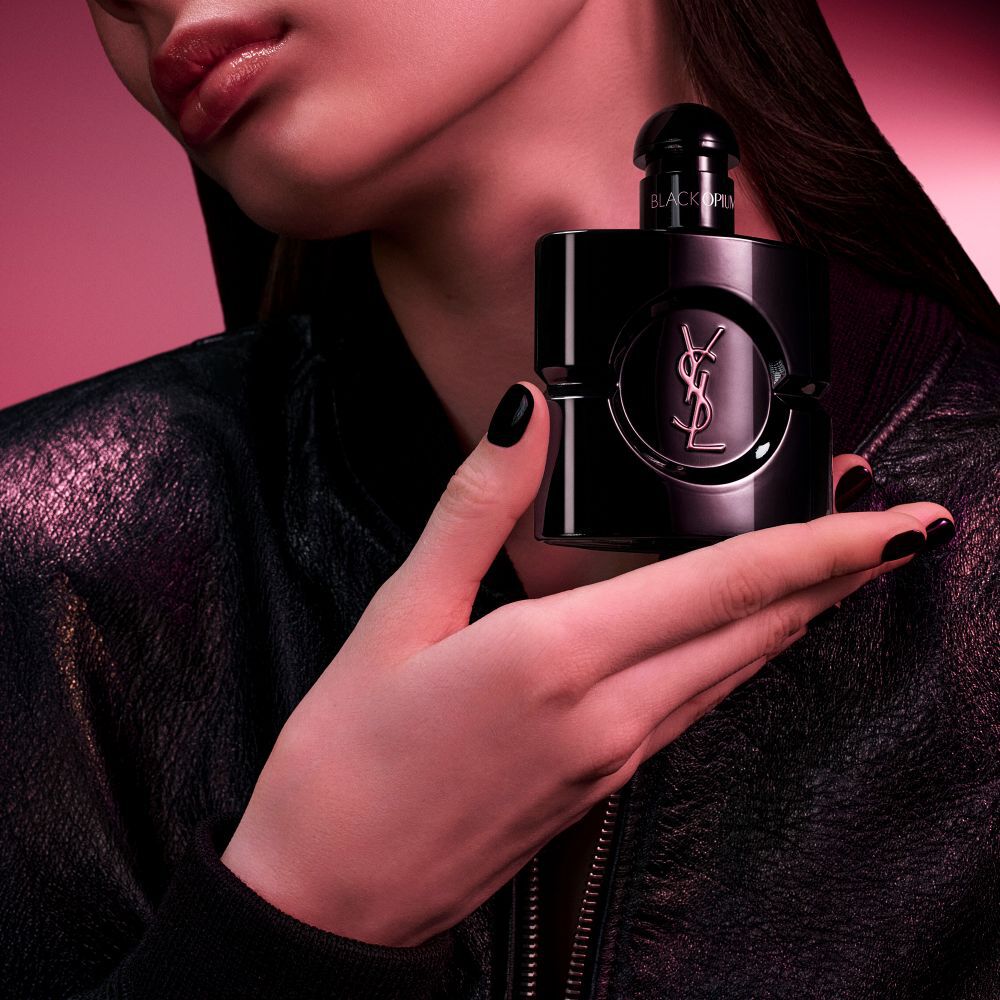 Flacon Black Opium Le Parfum en noir brillant, entoure de gousses de vanille sombre et de jasmin blanc, avec allegations.
