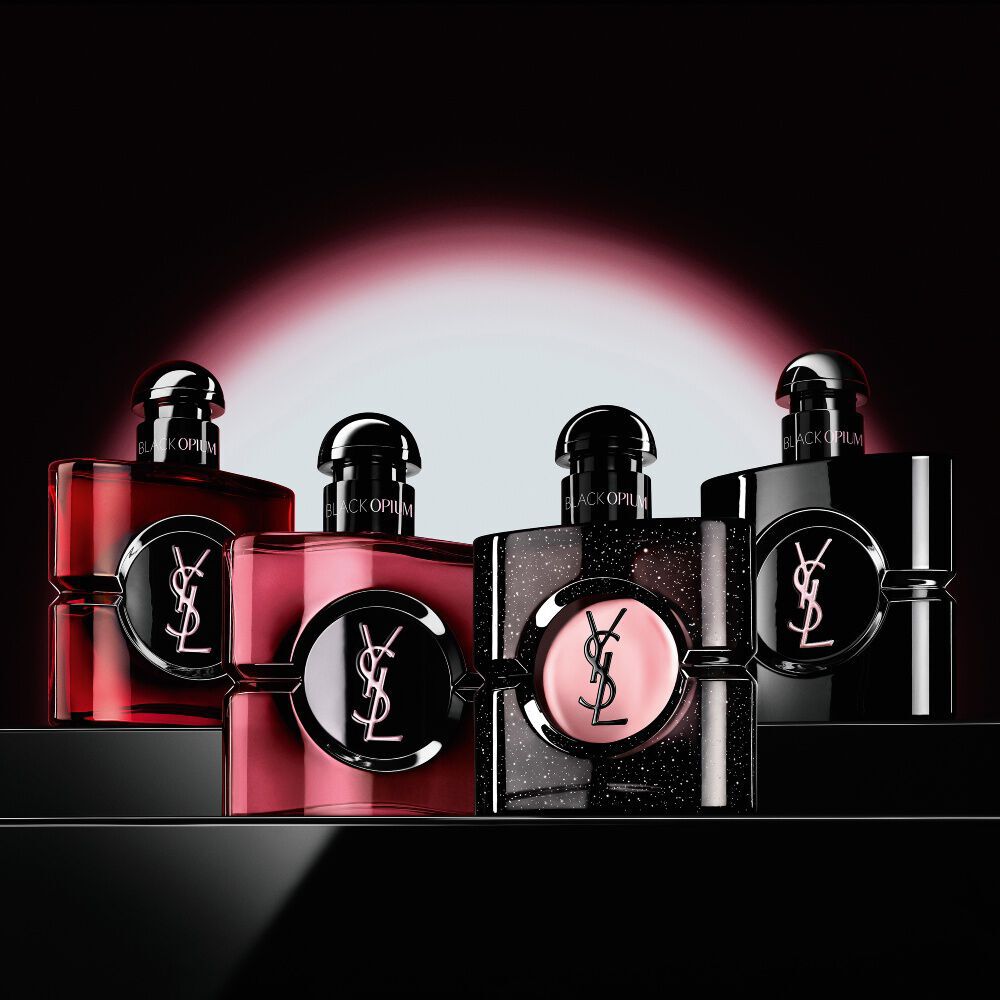 Quatre flacons de parfum Black Opium differents, alignes sur une surface sombre et reflechissante.