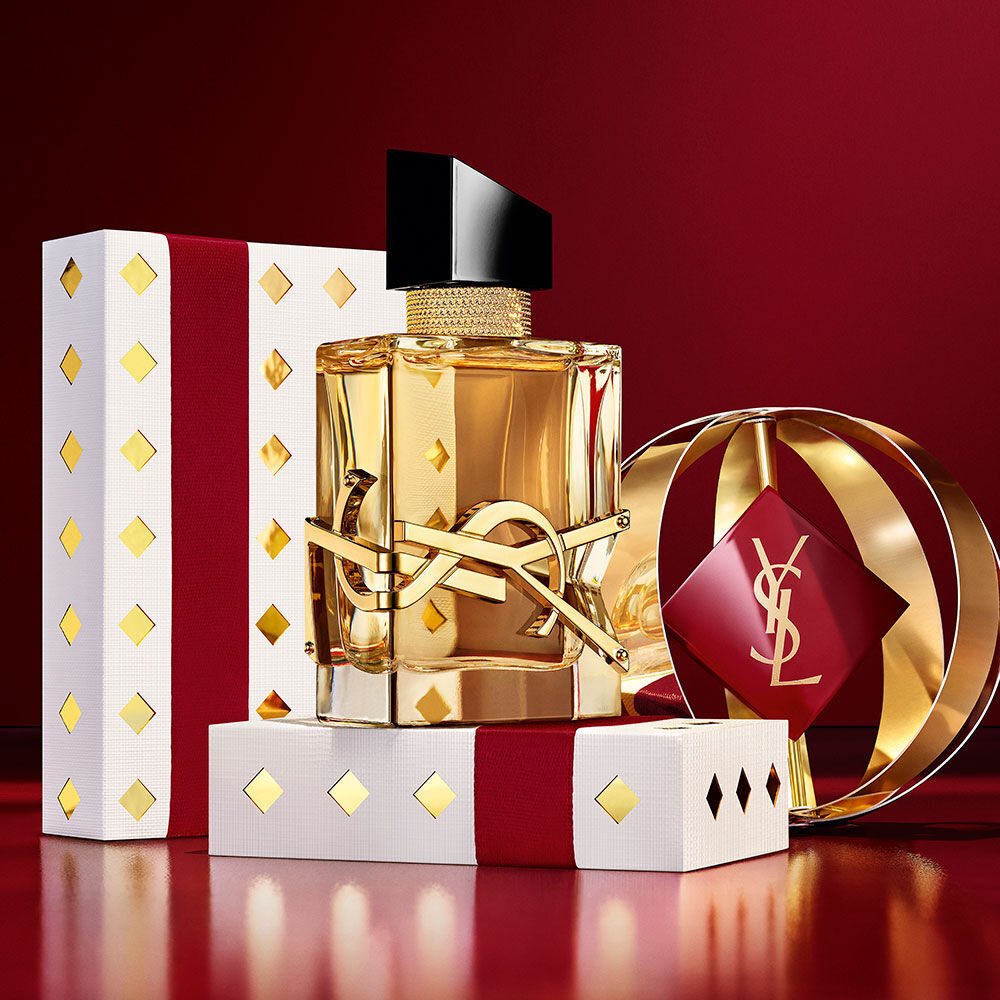 Flacon emblematique de LIBRE, mis en scene avec des coffrets cadeaux YSL luxueux aux tons bordeaux et or.