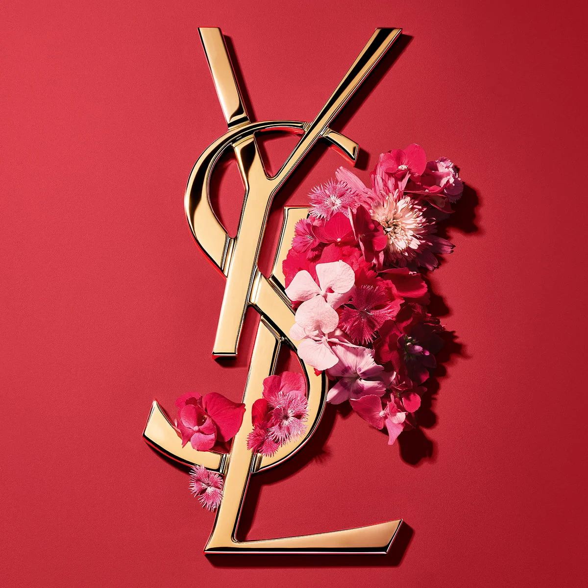 Logo Cassandre doré d'YSL, orné de fleurs printanières rose vif et présenté sur un fond rose.