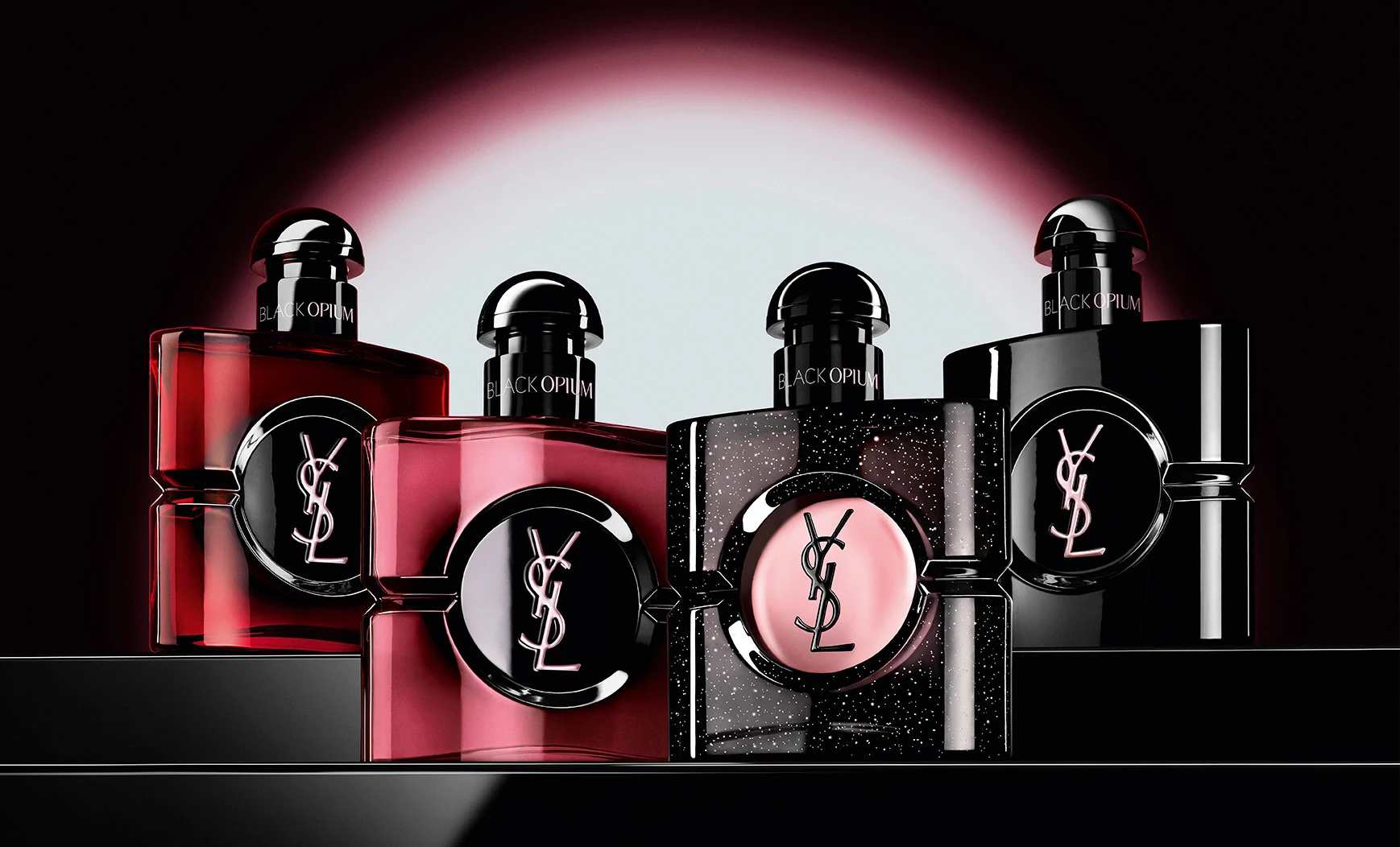 Quatre flacons différents de parfum Black Opium alignés sur une surface sombre et réfléchissante.