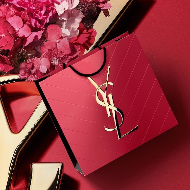 Sac shopping YSL rose orné du logo Cassandre doré, présenté à côté d'une composition florale rose.
