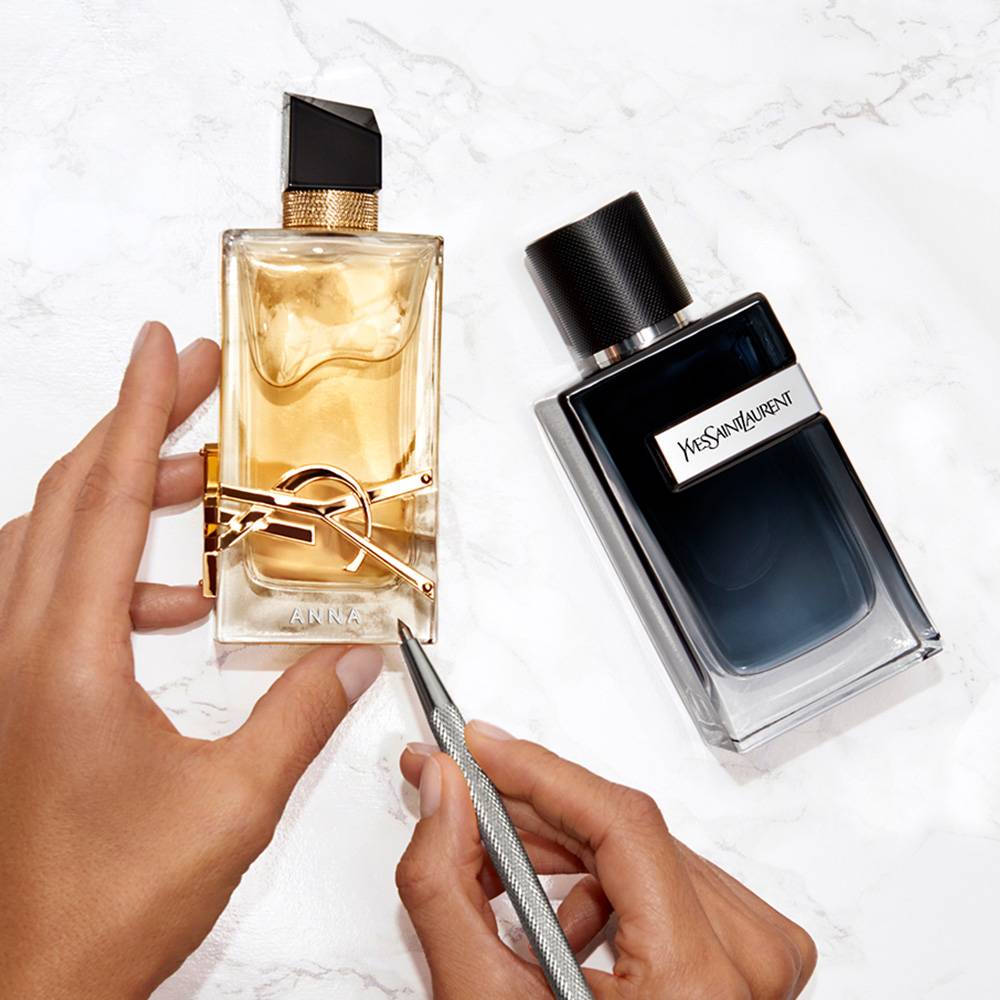 Deux flacons de parfum Yves Saint Laurent sur une surface en marbre, dont l'un est en cours de personnalisation avec le nom 