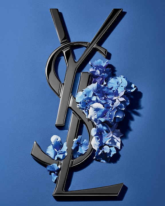 Logo Cassandre YSL noir orné de fleurs printanières d'un bleu éclatant, sur un fond bleu serein.