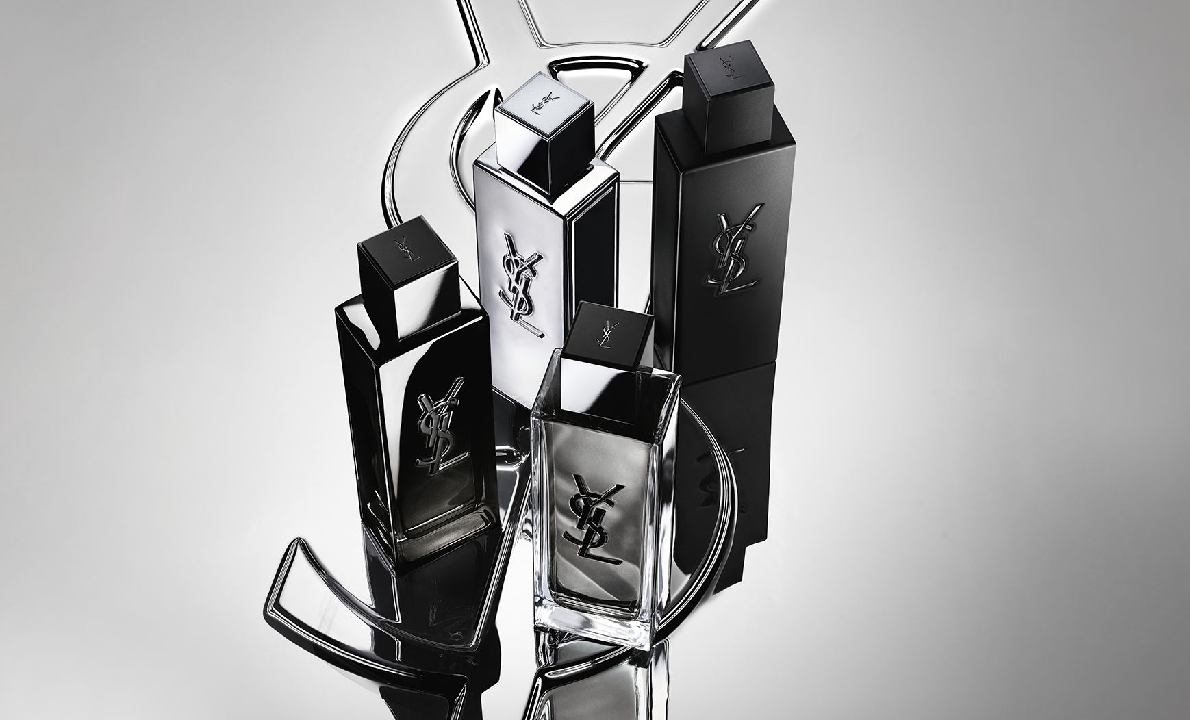 Photo de groupe de toute la gamme de parfums MYSLF, avec les flacons posés sur un grand logo Cassandre YSL à effet miroir réfléchissant.