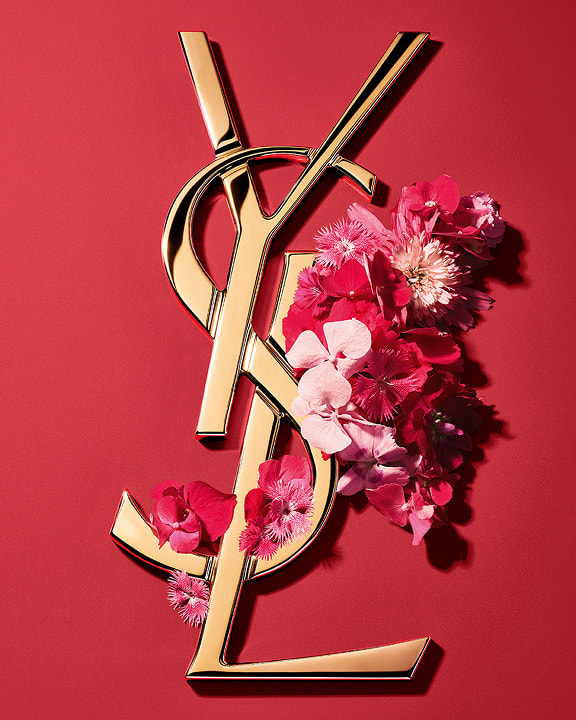 Logo Cassandre doré d'YSL, orné de fleurs printanières rose vif et présenté sur un fond rose.