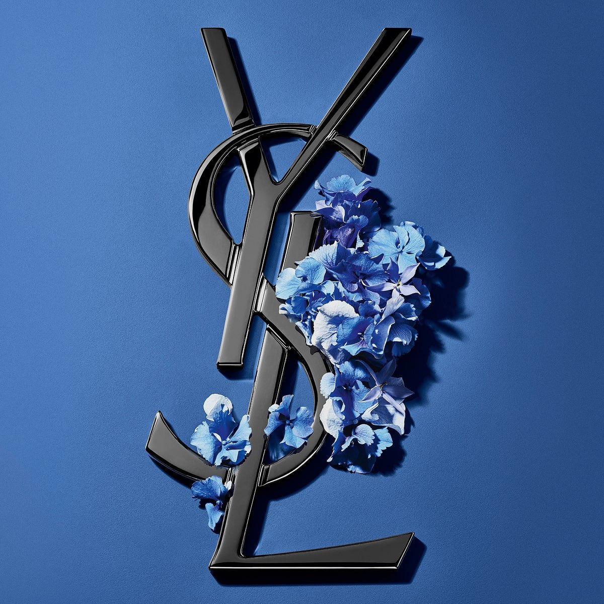 Logo Cassandre YSL noir orné de fleurs printanières d'un bleu éclatant, sur un fond bleu serein.