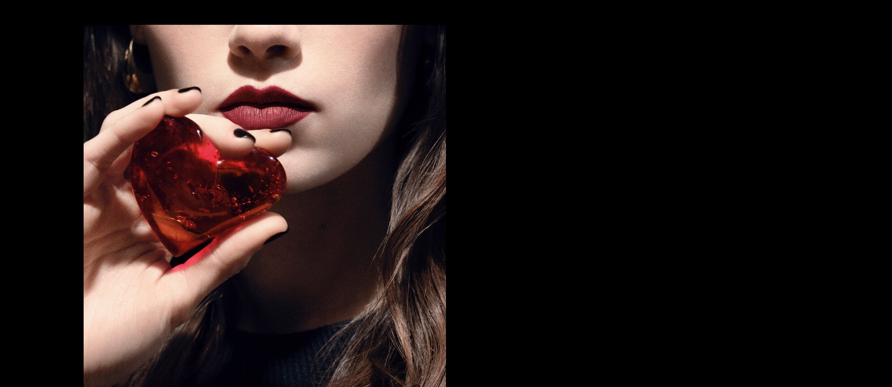 Gros plan sur les lèvres et la main d’un mannequin
tenant un bijou cœur translucide
rouge rubis pour YSL CŒUR Eau de Parfum.