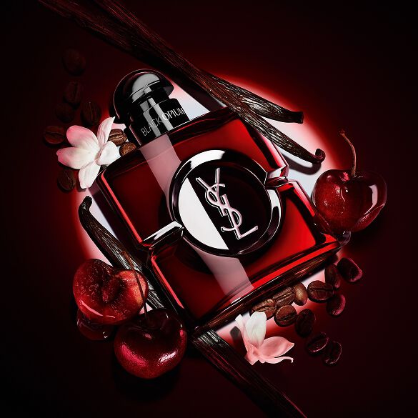 Flacon Black Opium Over Red en laque rouge profond, entouré de cerises rouges fraîches et de grains de café torréfiés.