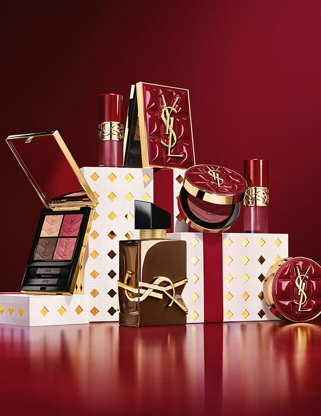 YSL Holiday 2026 makeup collection and fragrance set on gold-dotted white pedestals in burgundy.