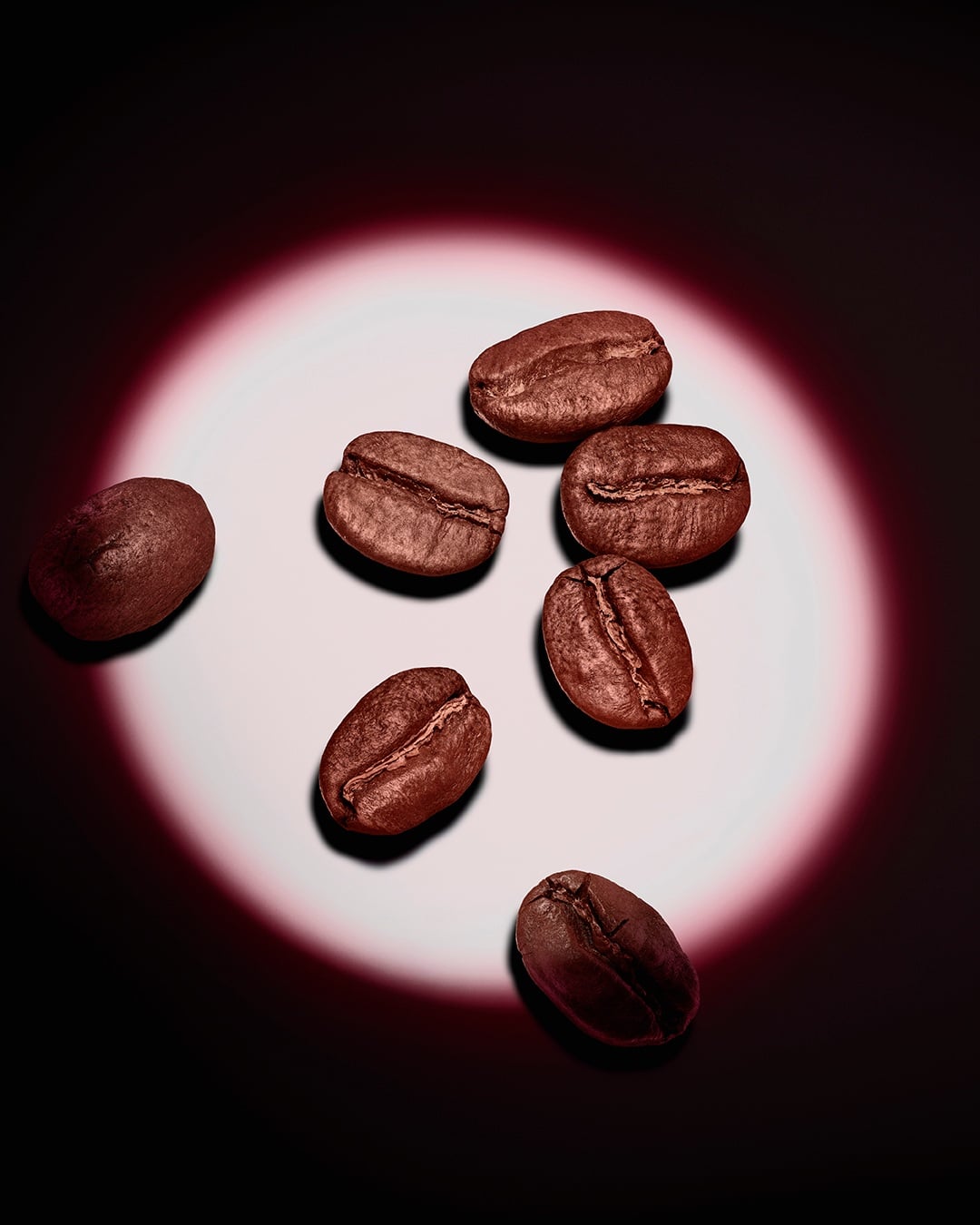 Un groupe de grains de café torréfiés, mis en lumière par un halo circulaire rose sur fond sombre.