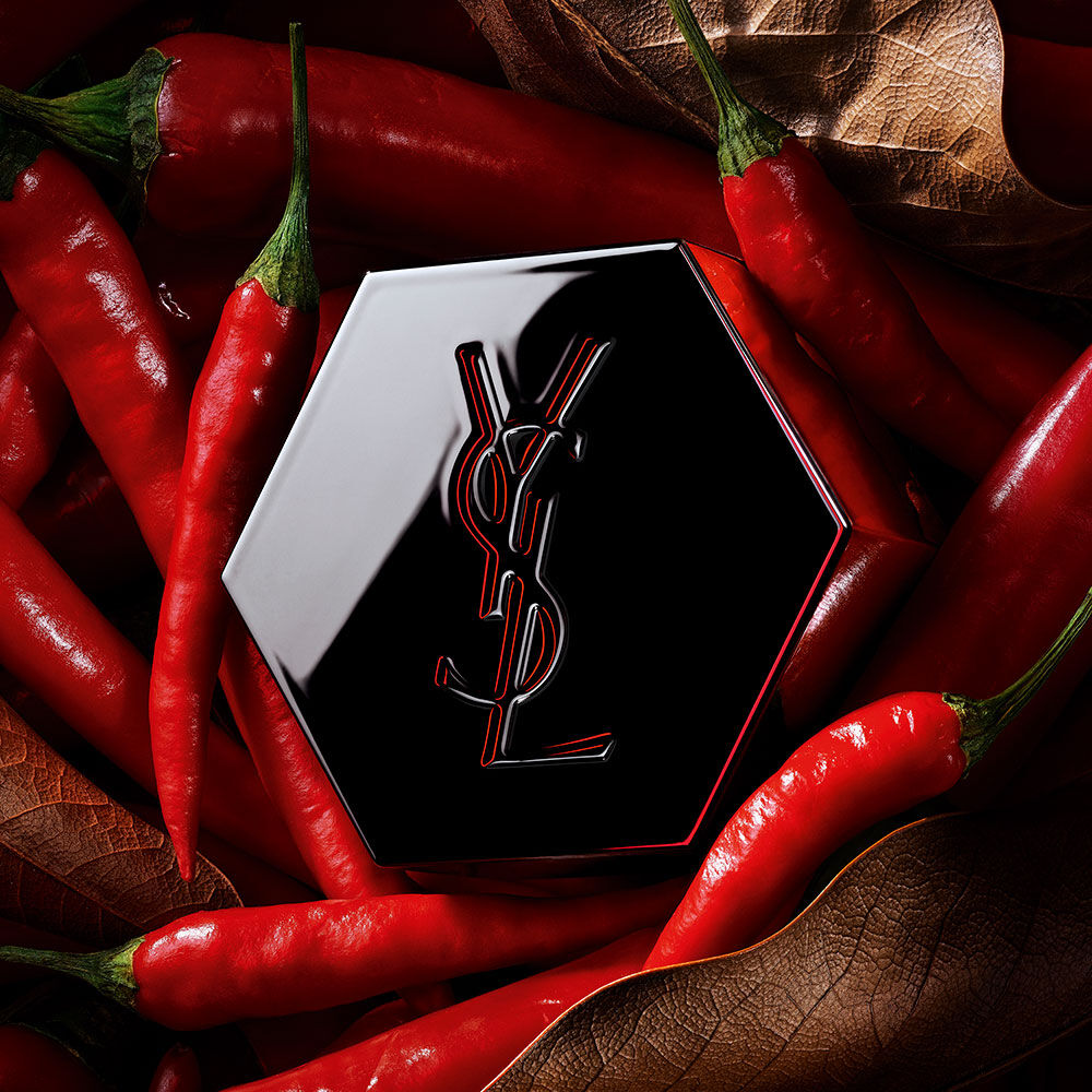Capot de parfum hexagonal noir YSL avec un logo aux contours rouges, entouré de piments rouges.