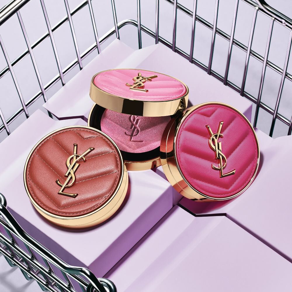 Trois blush poudres YSL Make Me Blush teintes 10, 12 et 66 présentés sur des blocs violets dans un panier métallique.