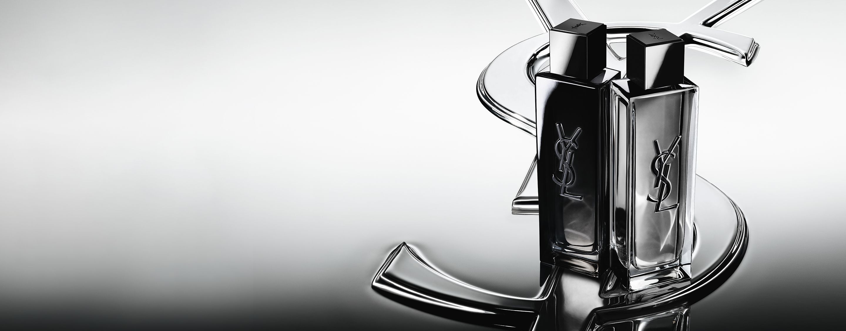 Les flacons de MYSLF Eau de Parfum et MYSLF Eau de Toilette Intense, côte à côte sur un grand logo Cassandre YSL à effet miroir.