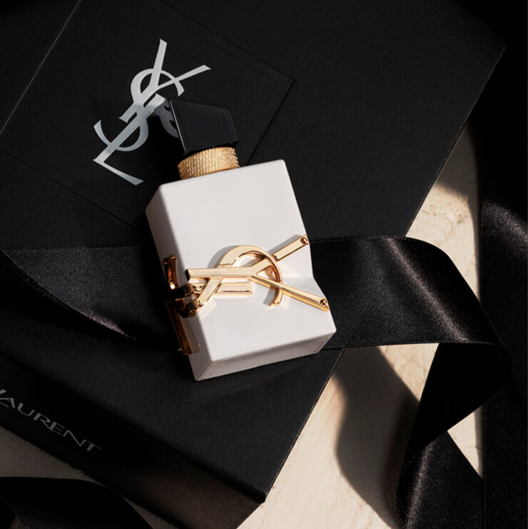 Un flacon blanc opaque élégant de Libre reposant sur un coffret cadeau YSL noir avec un ruban de soie.