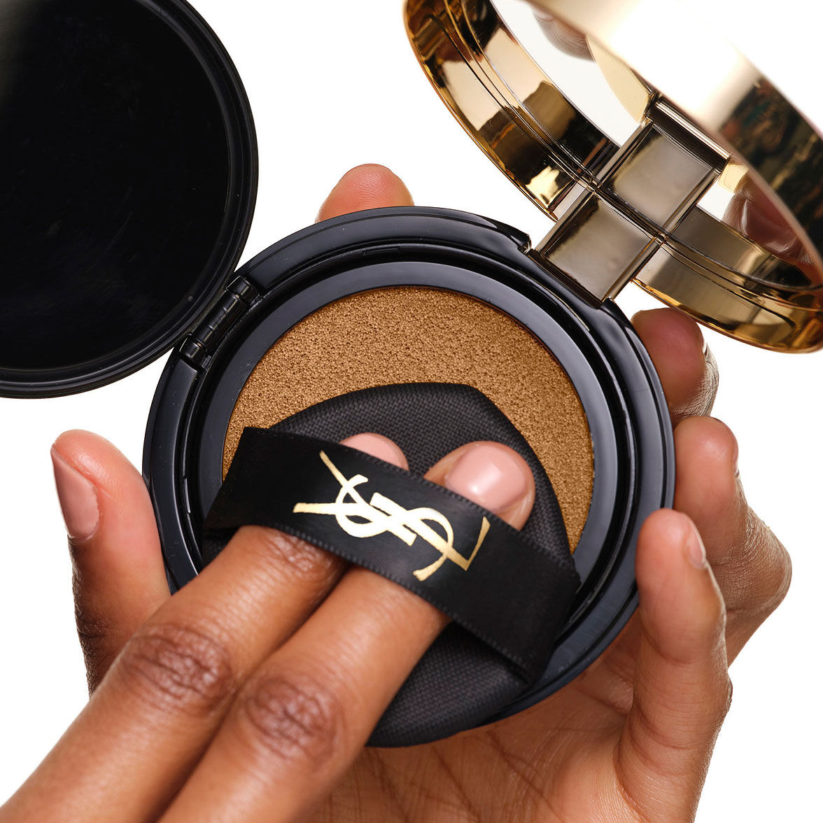 Chargement du YSL SKIN AFFAIR SOFT GLOW CUSHION. Doigts sous le ruban noir du logo, pressant le puff de maquillage.