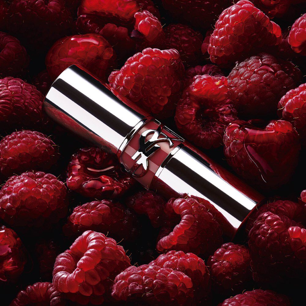 Rouge à lèvres YSL LOVESHINE Berry Crush, tube argenté avec logo YSL couleur baie, niché parmi des framboises fraîches.