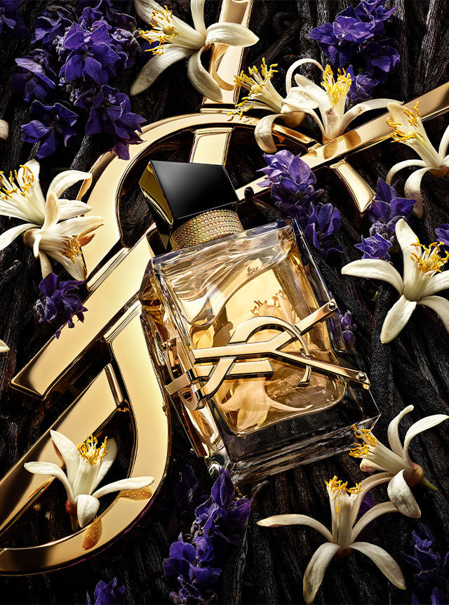 Le flacon de parfum Libre centré parmi un mélange de fleurs de lavande, de fleurs d'oranger et de gousses de vanille sur un fond doré YSL.
