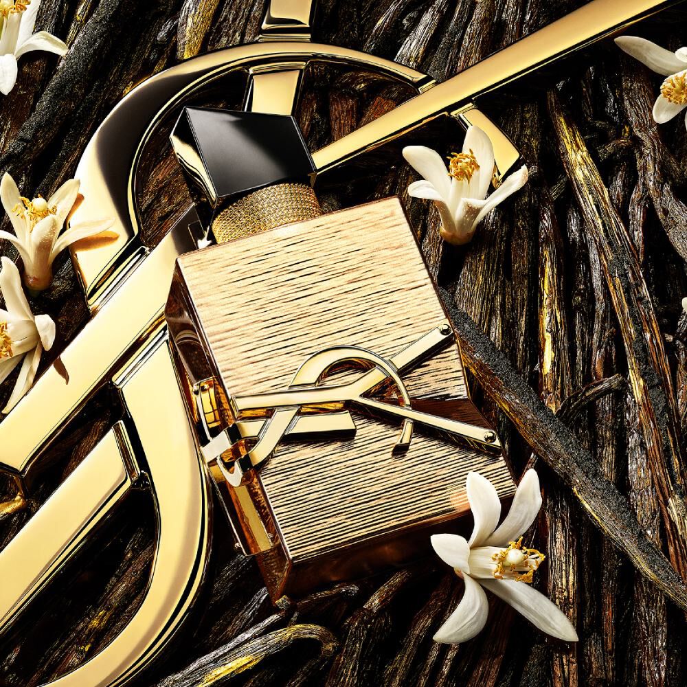 Un flacon de parfum doré avec un capuchon noir et le logo Yves Saint Laurent (YSL), sur un riche fond doré aux accents géométriques.