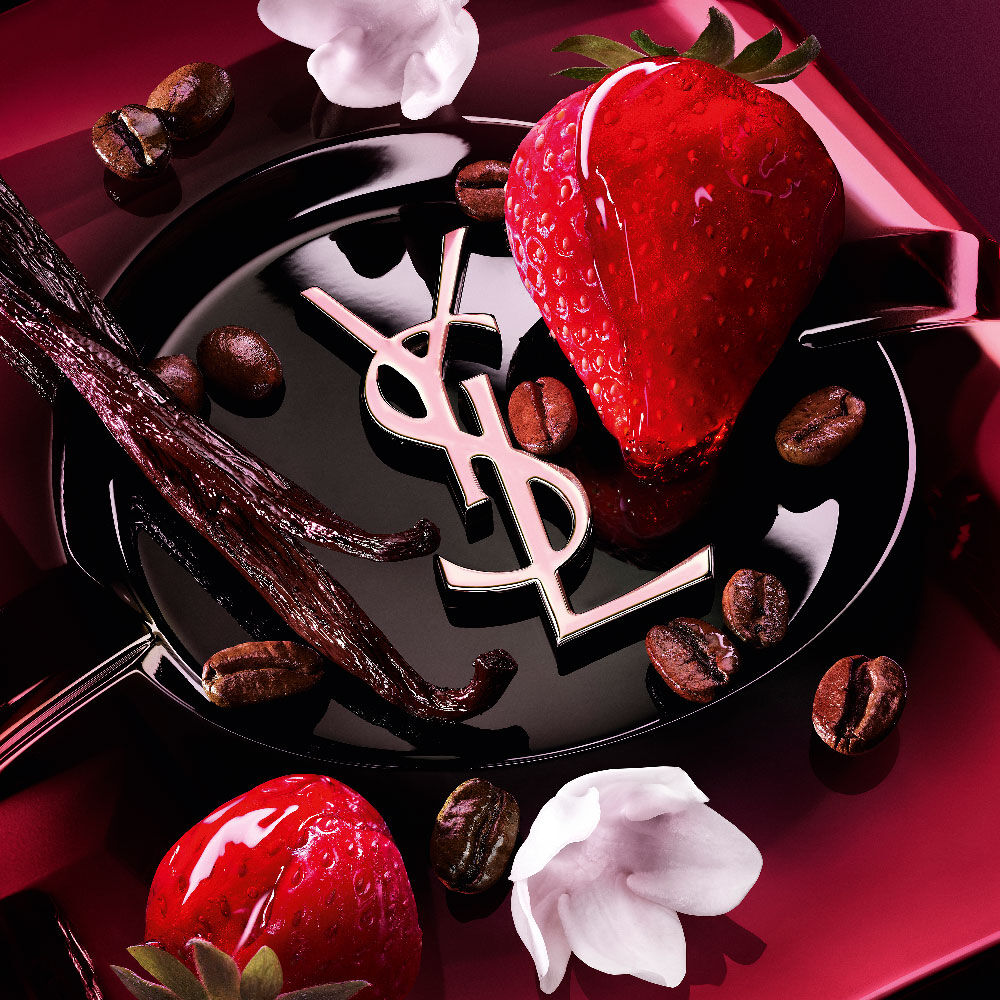 Gros
                plan sur des fraises fraîches, des gousses de vanille, des fleurs de jasmin et des
                grains de café torréfiés disposés autour du flacon de Black Opium Eau de Parfum Pink
                Glaze avec le cassandre emblématique de YSL.
