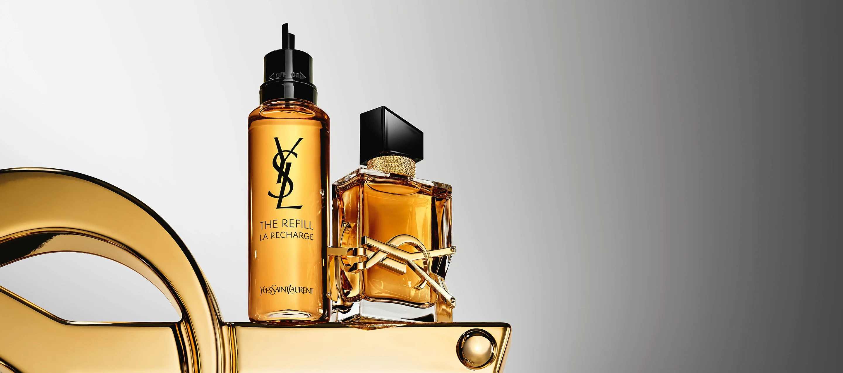 Deux flacons de parfum Yves Saint Laurent Libre, l'un une recharge, sur un présentoir doré.