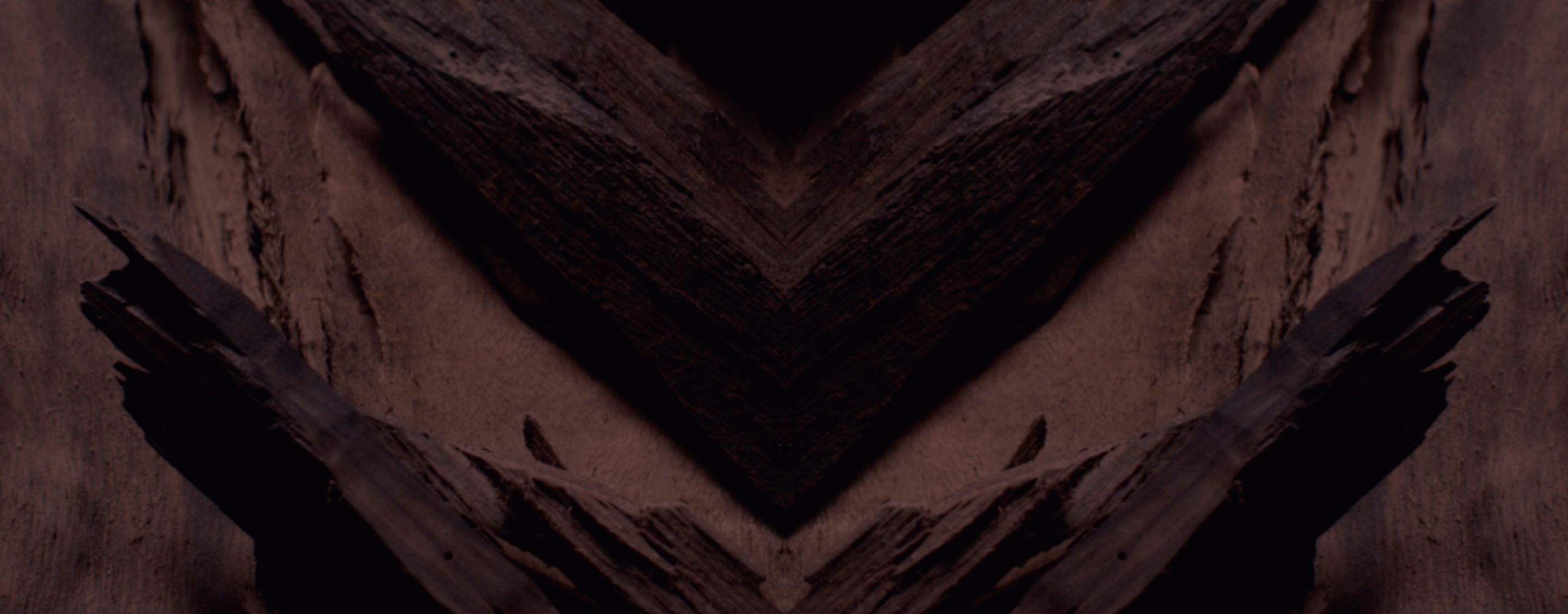 Dark, textured background with a prominent chevron pattern in
deep browns and blacks, designed for YSL LVP Extrait de Parfum
product display.