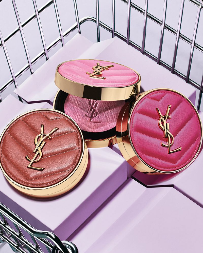 Trois blush poudres YSL Make Me Blush teintes 10, 12 et 66 présentés sur des blocs violets dans un panier métallique.