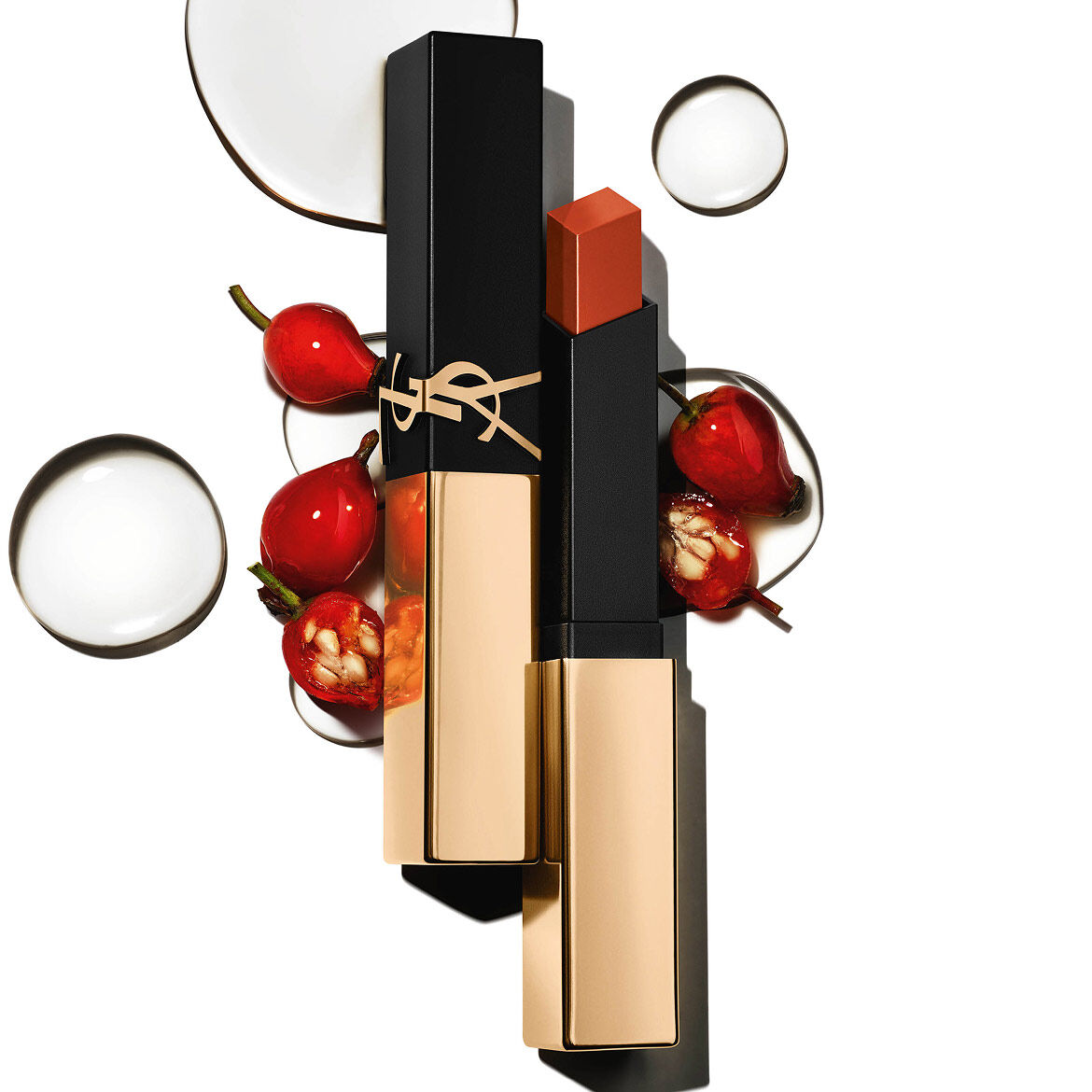 Rouge à lèvres YSL carré, capuchon doré, entouré de baies rouges et de gouttes claires sur fond blanc.